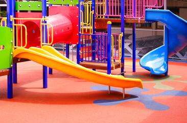 Colorful slides with tunnel and playground climbing equipment on rubber floor in outdoors playground area at kindergarten