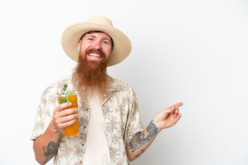 Redhead man with long beard drinking a cocktail on a beach isolated on white background pointing finger to the side