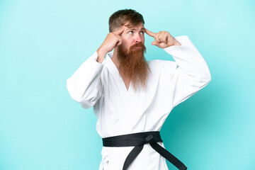 Redhead man with long beard doing karate isolated on blue background having doubts and thinking