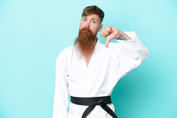 Redhead man with long beard doing karate isolated on blue background showing thumb down with...