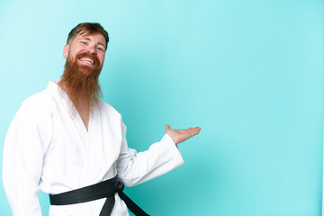 Redhead man with long beard doing karate isolated on blue background extending hands to the side...