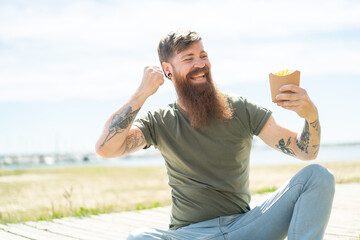 Redhead man with beard holding fried chips at outdoors celebrating a victory
