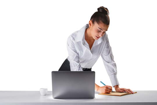 Concentrated young woman bending over desk writing, laptop beside, office work concept