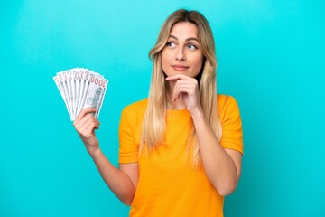 Young Uruguayan woman taking a lot of money isolated on blue background having doubts and thinking
