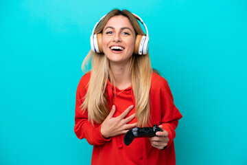 Young Uruguayan woman playing with a video game controller isolated on blue smiling a lot