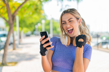 Young pretty sport woman at outdoors with phone in victory position - obrazy, fototapety, plakaty