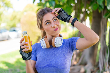 Young pretty sport woman holding an orange juice at outdoors having doubts and with confuse face...