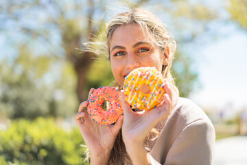 Young pretty blonde Uruguayan woman at outdoors holding donuts with happy expression