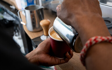Close up of barista pouring hot frothy steamed milk into delicious golden flat white at local...