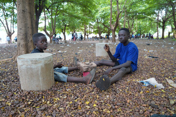 Two small black West African boys sitting in a public park busy playing tic tac toe with little...