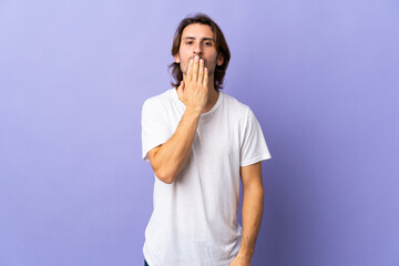 Young handsome man isolated on purple background covering mouth with hand