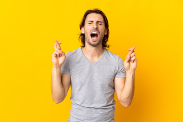 Young handsome man isolated on yellow background with fingers crossing