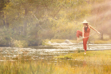 Woman with straw hat in middle of forest with river in background trees and nature warm colors, meditating in nature, traveling through east