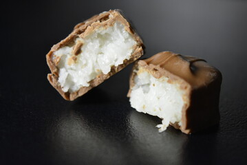 Pieces, slices of sweet coconut bar covered with milk chocolate placed on a black background.
