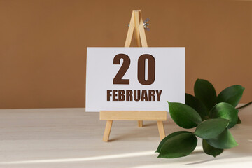 February 20th. Day 20 of month, Calendar date. Green branch, easel with the date and month on...