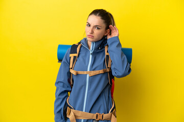 Young mountaineer woman with a big backpack over isolated yellow background having doubts