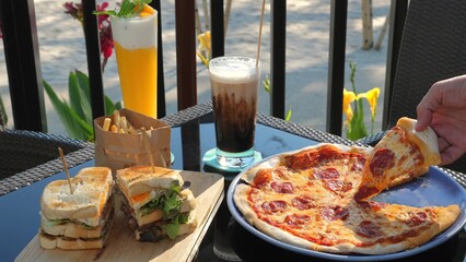 Al fresco dining scene with variety of popular foods including pizza, sandwiches, and french fries, complemented by refreshing beverages like beer and iced coffee. Casual outdoor eating and lifestyle.