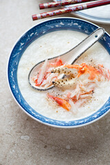 Bowl of asian congee or conjee with crab meat, vertical shot on a beige stone surface, middle closeup