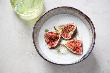 Bowl with greek yogurt and fresh torn fig fruits, horizontal shot on a light-beige stone background, elevated view