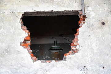 Large hole in an old brick wall. There's a lantern hanging behind the wall - 739152022