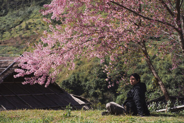 travel and work concept with solo freelancer man sit under cherry blossom tree and relax with layer...