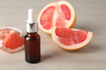 Grapefruit essential oil in bottle and fruit on light wooden table, closeup. Space for text