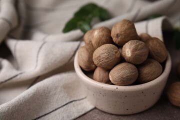 Whole nutmegs in bowl on brown table, closeup. Space for text