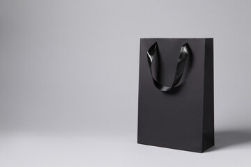 Black paper bag on light grey background, space for text