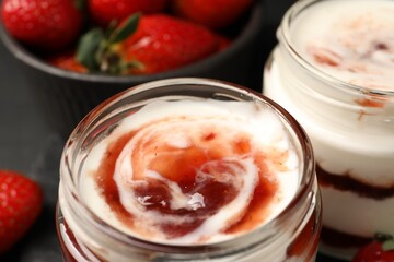 Tasty yoghurt with jam and strawberries on black table, closeup