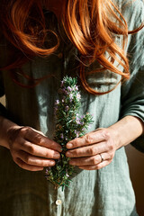 Redhead Woman holding in her hands a bunch of blooming rosemary. Herbalist woman preparing fresh...