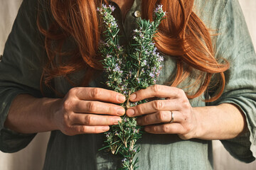 Redhead Woman holding in her hands a bunch of blooming rosemary. Herbalist woman preparing fresh...