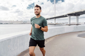 Man running by the river with a bridge in the background, focused on his fitness.