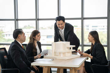 Fototapeta premium Asian businessman talking with team in meeting room. They dissing about building model and design together.