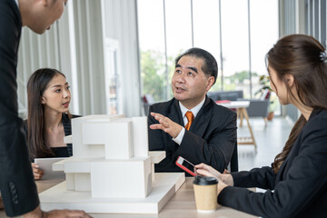 Group of business professionals gathers around a table, engaging in lively discussion while examining a detailed building model.