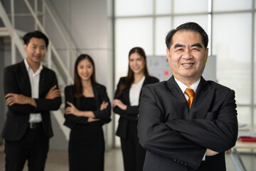 Portrait senior businessman standing in front of team in office. He looking to camera with smile with team. Teamwork and success concept.