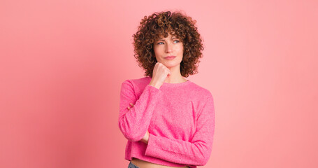 Thoughtful young woman touching face on pink background