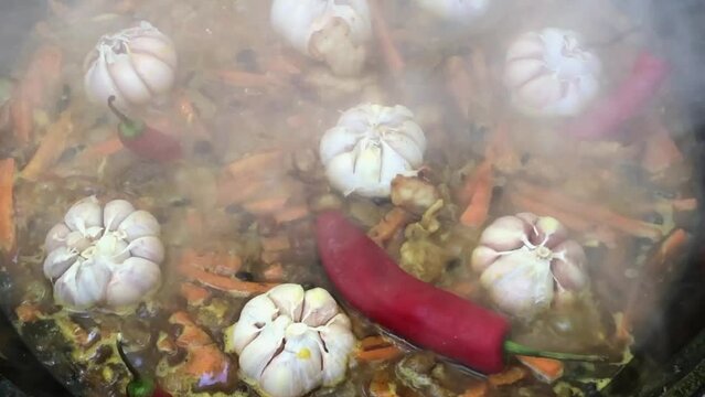 High angle real time of appetizing pilaf cooking with garlics and red peppers in pan with hot steam