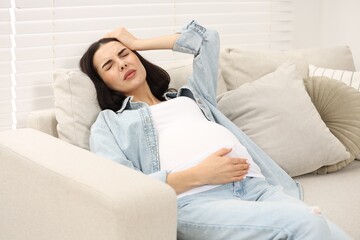 Pregnant woman suffering from headache on sofa at home