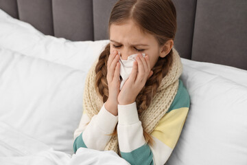 Sick girl with tissue coughing on bed at home