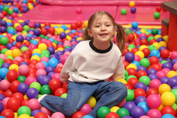 Fototapeta na wymiar Happy little girl sitting on colorful balls in ball pit