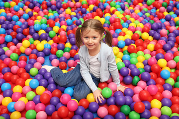 Fototapeta na wymiar Happy little girl sitting on colorful balls in ball pit