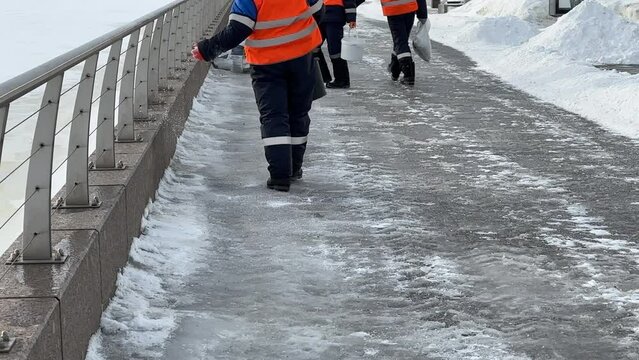 Workers spreading salt to slipper sidewalk. Winter road treatment with de-icing reagent, prevent slipping on road. Sprinkle technical salt on paving slabs to remove ice and prevent slipping accident. 