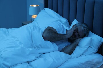 Mature man suffering from headache in bed at night