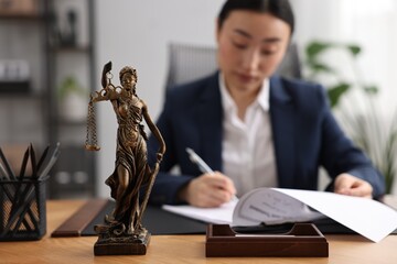Notary signing document at table in office, focus on Lady Justice statue - obrazy, fototapety, plakaty