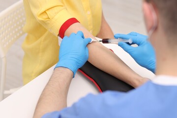 Doctor taking blood sample from patient with syringe at white table in hospital, closeup