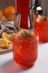 Aperol spritz cocktail, ice cubes, rosemary and orange slices in glass on white wooden table, closeup