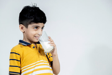 Indian kid with glass of milk in hand having a sip of milk on isolated background