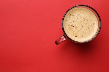 Fresh coffee in cup on red background, top view. Space for text