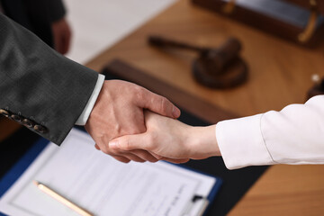 Obraz premium Notary shaking hands with client at wooden table in office, closeup