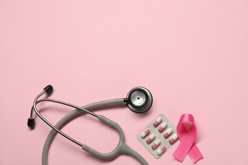 Fototapeta premium Breast cancer awareness. Pink ribbon, stethoscope and pills on color background, flat lay. Space for text